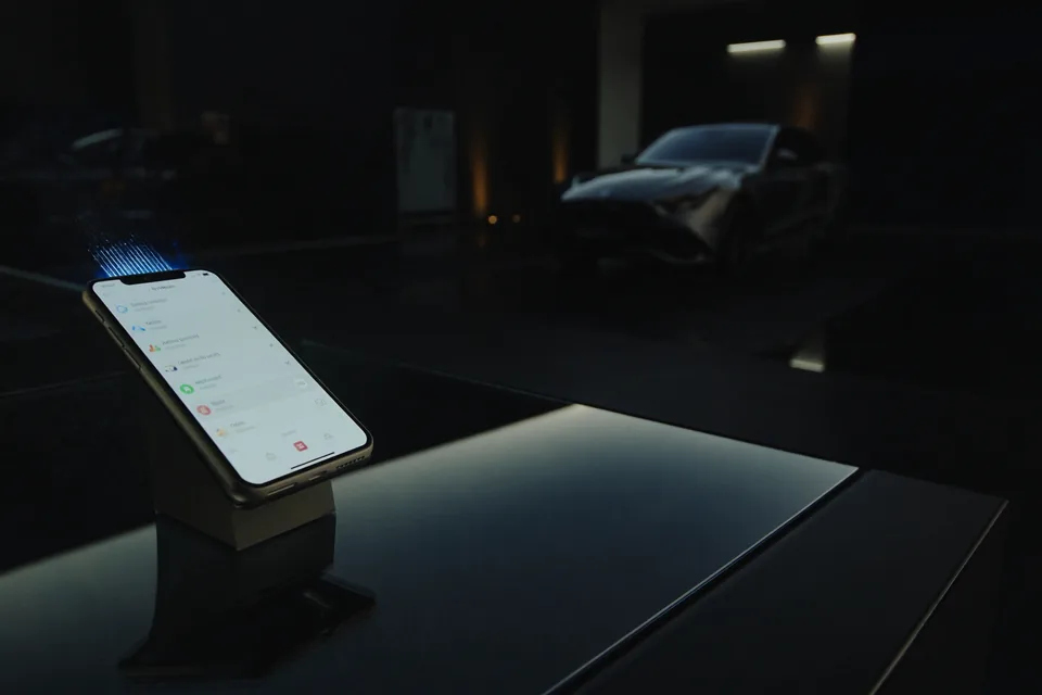 A phone on a stand in a dark car showroom, a car behind it, light streaming from the phone