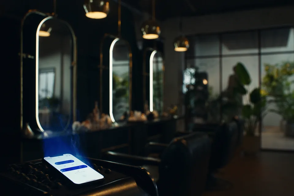 A phone glowing on a salon chair in front of a row of lit mirrors